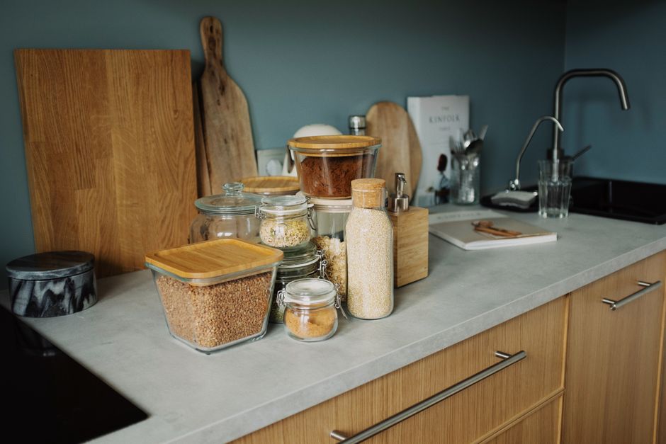 A minimalist kitchen setup features neatly arranged glass jars and wooden kitchenware on a contemporary countertop.