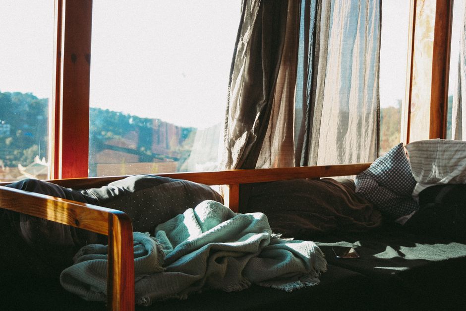 Sunlight streaming through curtains onto a cozy bed with blankets and pillows in a serene room.